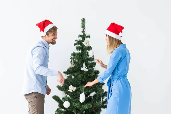 Ünnepek és ünnepi koncepció - Fiatal család pár télapó kalapban díszíti a karácsonyfát — Stock Fotó