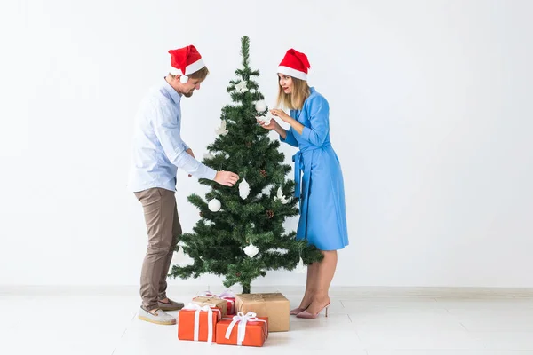 Férias e conceito festivo - Jovem casal familiar em chapéus de Santa decorar a árvore de Natal — Fotografia de Stock