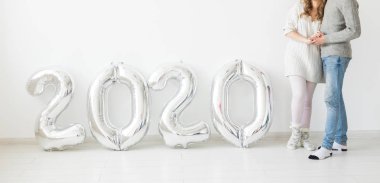 Bayramlar, şenlik ve parti konsepti - Beyaz arka planda gümüş 2020 balon yakınında mutlu bir çift. Yeni yıl kutlaması, yakın plan.