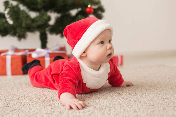 Милая малышка в костюме Санта Клауса ползает по полу над елкой. Праздничный сезон
.