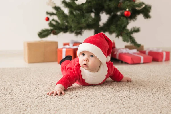 可爱的女婴穿着圣爪西服爬到圣诞树上的地板上。 假日季节. — 图库照片