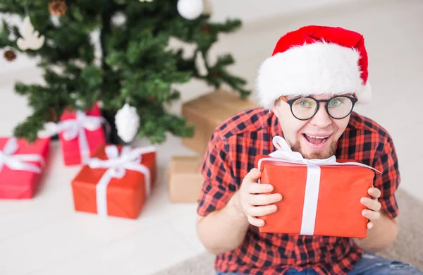 Concepto de Navidad y vacaciones - Hombre divertido en sombrero de santa celebración de un regalo en casa en la sala de estar —  Fotos de Stock