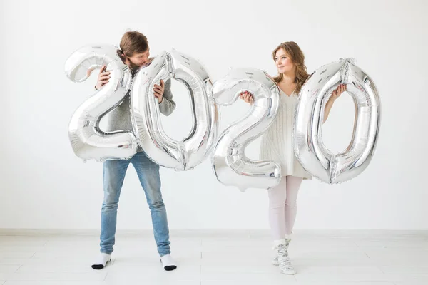 Vacaciones, festivo y concepto de fiesta - Feliz pareja cariñosa besa y sostiene globos de plata 2020 sobre fondo blanco. Celebración de Año Nuevo — Foto de Stock