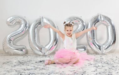 Yeni yıl, tatiller ve kutlama konsepti - 2020 numaralı balonlarla birlikte oturan küçük kız