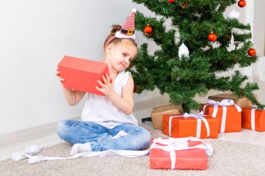 Çocuk Noel hediyelerini açıyor. Noel ağacının altında hediye kutularıyla çocuk.