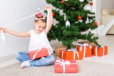 Çocuk Noel hediyelerini açıyor. Noel ağacının altında hediye kutularıyla çocuk.