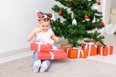 Çocuk Noel hediyelerini açıyor. Noel ağacının altında hediye kutularıyla çocuk.