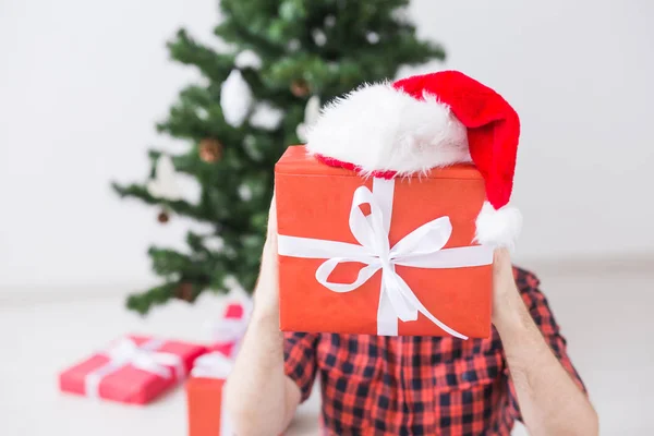 圣诞和假日的概念- -一个戴着圣诞礼帽、在客厅里拿着礼物的有趣男人 — 图库照片