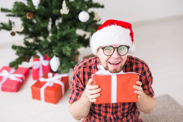 圣诞节和假日的概念- -一个戴着圣诞礼帽、在客厅里拿着礼物的有趣男人 — 图库照片