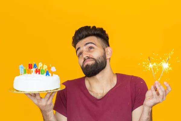 Portret zabawny pozytywny facet trzyma gratulacyjny domowej roboty ciasto w dłoniach na żółtym tle. Koncepcja i zabawa i uroczystość. — Zdjęcie stockowe
