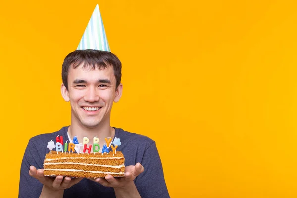 Elinde yanan bir mum tutan gözlük ve kopya alanı ile sarı bir arka plan üzerinde bir tebrik ev yapımı pasta ile Crazy neşeli genç Asya adam. Doğum günü ve yıldönümü kutlamaları — Stok fotoğraf