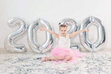 Yeni yıl, tatiller ve kutlama konsepti - 2020 numaralı balonlarla birlikte oturan küçük kız