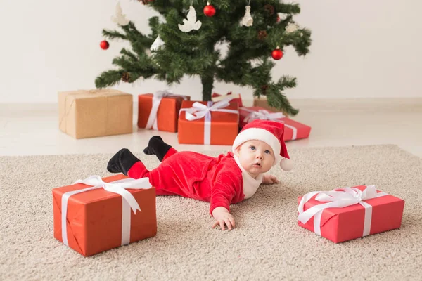 Carina la bambina che indossa la tuta di Babbo Natale strisciando sul pavimento sopra l'albero di Natale. Stagione delle vacanze . — Foto Stock