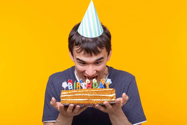 Divertente ragazzo positivo in occhiali tiene tra le mani una torta fatta in casa con l'iscrizione buon compleanno in posa su uno sfondo giallo. Concetto di vacanze e anniversari . — Foto Stock