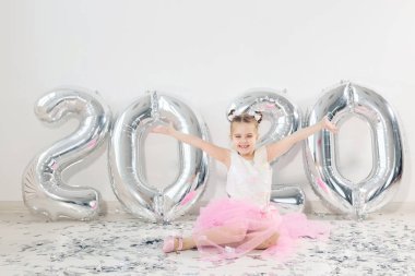 Yeni yıl, tatiller ve kutlama konsepti - 2020 numaralı balonlarla oturan çocuk