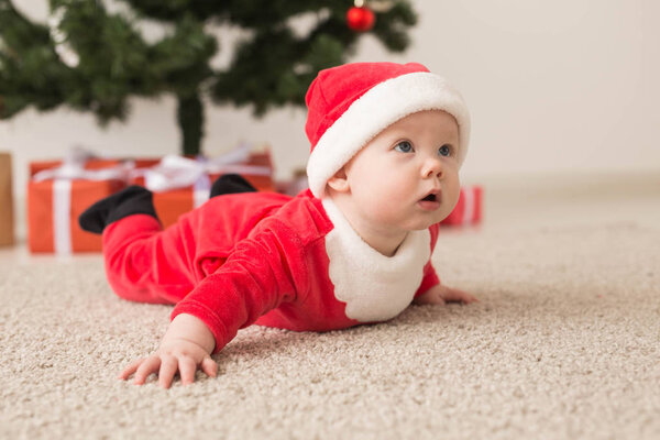 Милая малышка в костюме Санта Клауса ползает по полу над елкой. Праздничный сезон
.