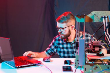 Laboratuvarda 3D yazıcı kullanan ve ürün prototipi, teknoloji ve yenilik kavramını inceleyen genç bir erkek tasarımcı.