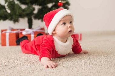 Noel Baba kostümü giyen tatlı bir bebek Noel ağacının üzerinde sürünüyor. Tatil sezonu.
