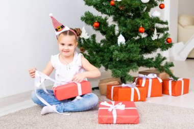 Çocuk Noel hediyelerini açıyor. Noel ağacının altında hediye kutularıyla çocuk.