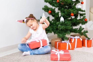 Çocuk Noel hediyelerini açıyor. Noel ağacının altında hediye kutularıyla çocuk.