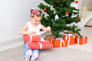 Çocuk Noel hediyelerini açıyor. Noel ağacının altında hediye kutularıyla çocuk.