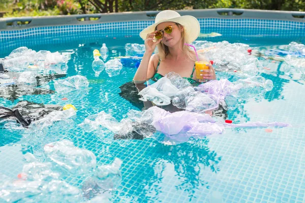 Probleem van afval, plastic recycling, vervuiling en milieu concept-domme vrouw zwemt en plezier hebben in een vervuild zwembad. Flessen en plastic zakken zweven in de buurt van haar — Stockfoto