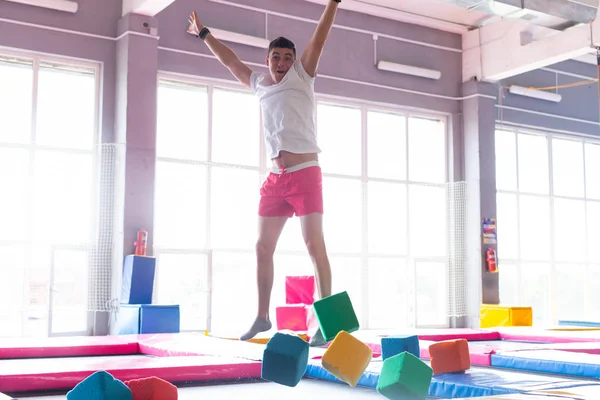 Fitness, diversión, ocio y deporte concepto de actividad - Hombre feliz guapo saltando en un trampolín en el interior — Foto de Stock