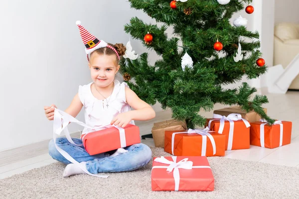 Kid opening Xmas presents. Child under Christmas tree with gift boxes.