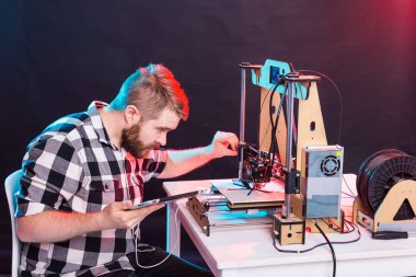 Laboratuvarda 3D yazıcı kullanan ve ürün prototipi, teknoloji ve yenilik kavramını inceleyen genç bir erkek tasarımcı.