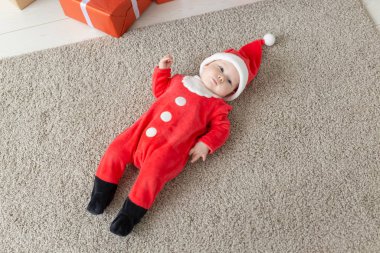 Güzel küçük bebek Noel 'i kutluyor. Yeni yıl tatili. Noel kostümü içindeki komik bebek ve Noel Baba şapkası, üst manzara