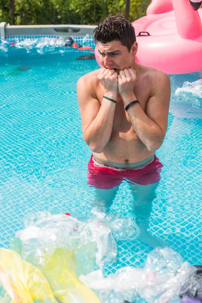 Ecology, plastic trash, environmental emergency and water pollution - shocked man standing in a dirty swimming pool