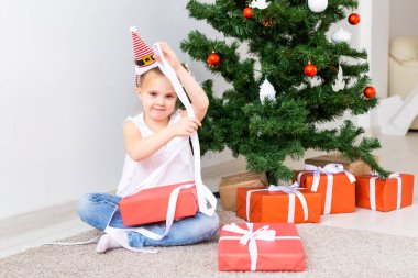 Çocuk Noel hediyelerini açıyor. Noel ağacının altında hediye kutularıyla çocuk.