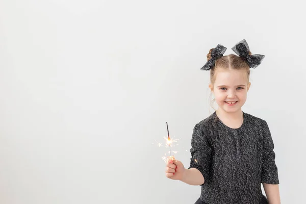 Vacaciones, navidad y concepto de año nuevo: la niña feliz sostiene una chispa ardiente en su mano sobre un fondo blanco con espacio para copiar — Foto de Stock