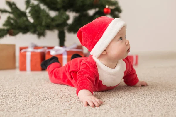 Linda niña con traje de Santa Claus arrastrándose por el suelo sobre el árbol de Navidad. Temporada de vacaciones . — Foto de Stock