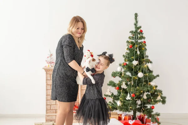 Urlaub und Haustier-Konzept - Mutter und Tochter spielen zu Hause mit Jack Russell Terrier-Hund vor dem Weihnachtsbaum — Stockfoto