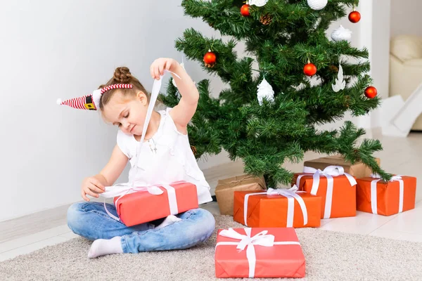 Çocuk Noel hediyelerini açıyor. Noel ağacının altında hediye kutularıyla çocuk.