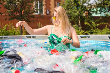 Çöp sorunu, plastik geri dönüşüm, kirlilik ve çevre kavramı - aptal kadın yüzer ve kirli bir havuzda eğlenin. Şişeler ve plastik torbalar onun yanında yüzer.