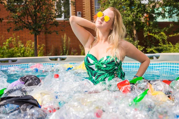 Problème des déchets, du recyclage du plastique, de la pollution et du concept environnemental : la femme idiote nage et s'amuse dans une piscine polluée. Bouteilles et sacs en plastique flottent près d'elle — Photo