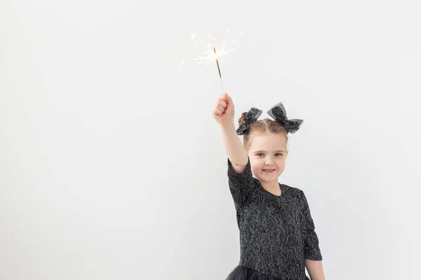 Vacaciones, navidad y concepto de año nuevo: la niña feliz sostiene una chispa ardiente en su mano sobre un fondo blanco con espacio para copiar — Foto de Stock