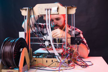 Laboratuvarda 3D yazıcı kullanan ve ürün prototipi, teknoloji ve yenilik kavramını inceleyen genç bir erkek tasarımcı.