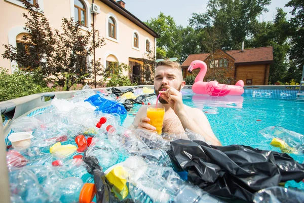 ゴミの問題、プラスチックのリサイクル、汚染と環境の概念-愚かな男は泳ぎ、汚染されたプールで楽しみを持っています。近くにはペットボトルやビニール袋が浮かんでいる。 — ストック写真