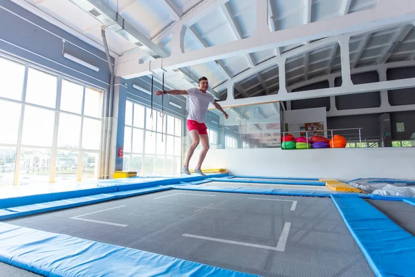 Fitness, diversão, lazer e esporte conceito de atividade - Bonito homem feliz pulando em um trampolim dentro de casa — Fotografia de Stock