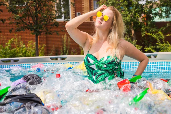 ゴミ、プラスチックリサイクル、汚染と環境の概念の問題 - 愚かな女性が泳ぎ、汚染されたプールで楽しみを持っています。ボトルとビニール袋は彼女の近くに浮かぶ — ストック写真