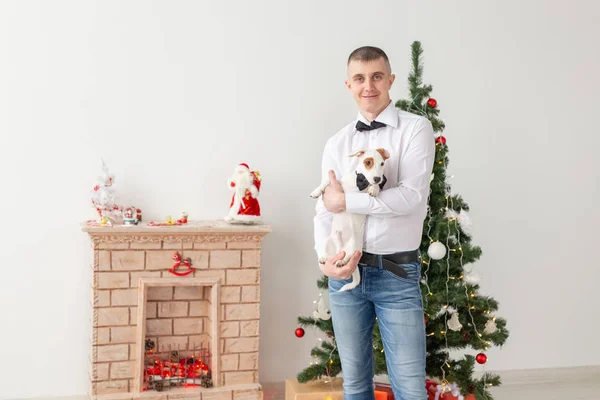 Urlaub und Haustier-Konzept - glücklicher Mann und Hund zu Hause mit Weihnachtsbaum — Stockfoto