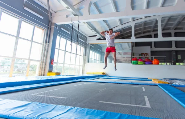 Fitness, diversión, ocio y deporte concepto de actividad - Hombre feliz guapo saltando en un trampolín en el interior — Foto de Stock