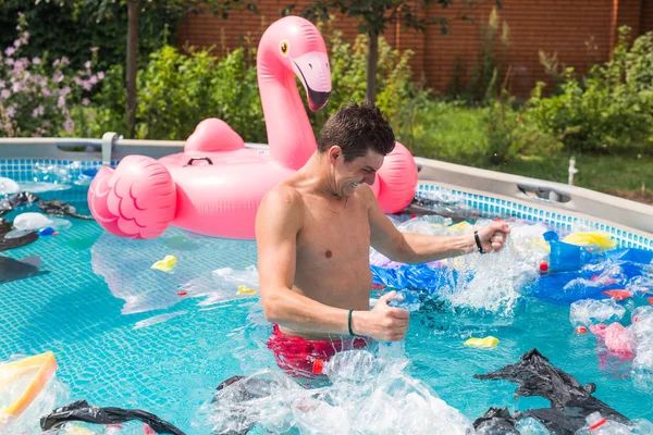 Ecology, plastic trash, environmental emergency and water pollution - shocked man standing in a dirty swimming pool