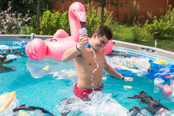 Ecology, plastic trash, environmental emergency and water pollution - shocked man standing in a dirty swimming pool