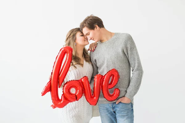 Giorno di San Valentino, vacanza e idea regalo. Felice giovane coppia caucasica in possesso di parola d'amore a forma di palloncino rosso su sfondo bianco — Foto Stock