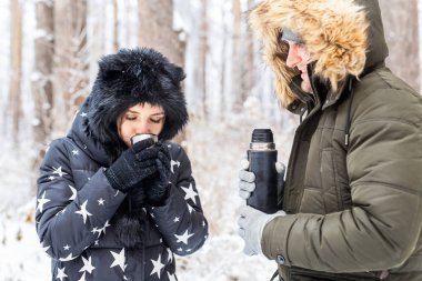 Birbirine aşık genç bir çift termostan sıcak bir içecek içer ve kış doğasının tadını çıkarır..