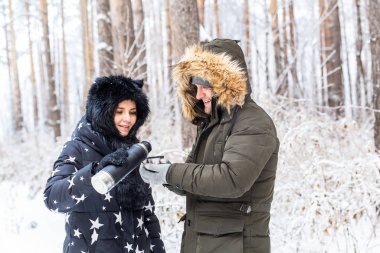 Mevsim ve yürüyüş konsepti - Mutlu çift kış ormanında sıcak çay içiyor